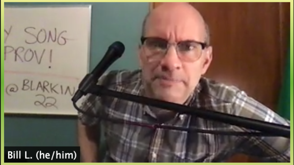 A bald man in a plaid shirt at a microphone staring into the camera.