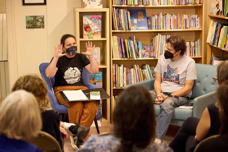 A person in a rat T-shirt talking with animation to a man in a 'Cat Ladies for Kamala' T-shirt while a crowd listens attentively