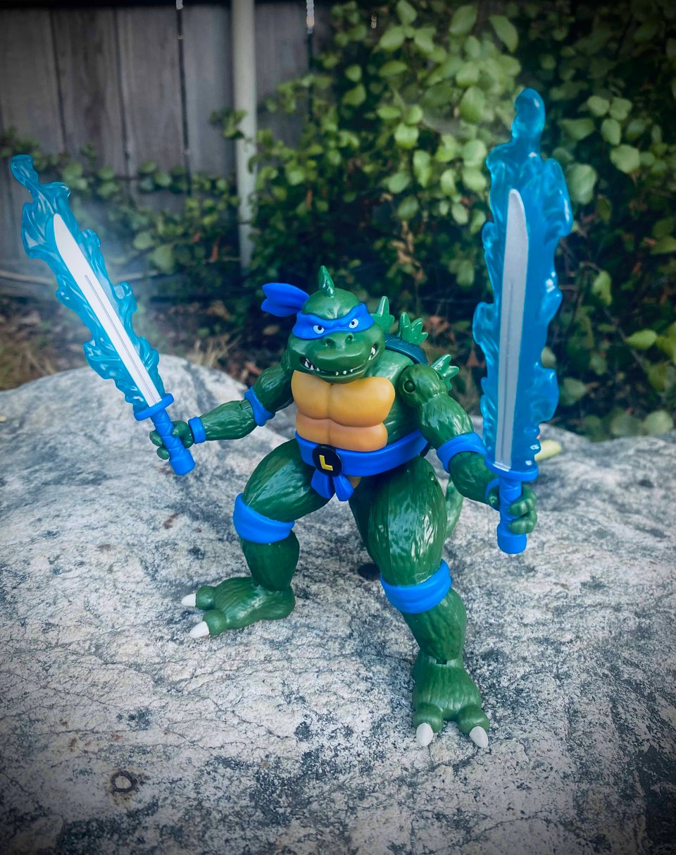 Photo of a Playmates Ninja Turtle action figure that merges Leonardo with Godzilla standing on a rock in a backyard.