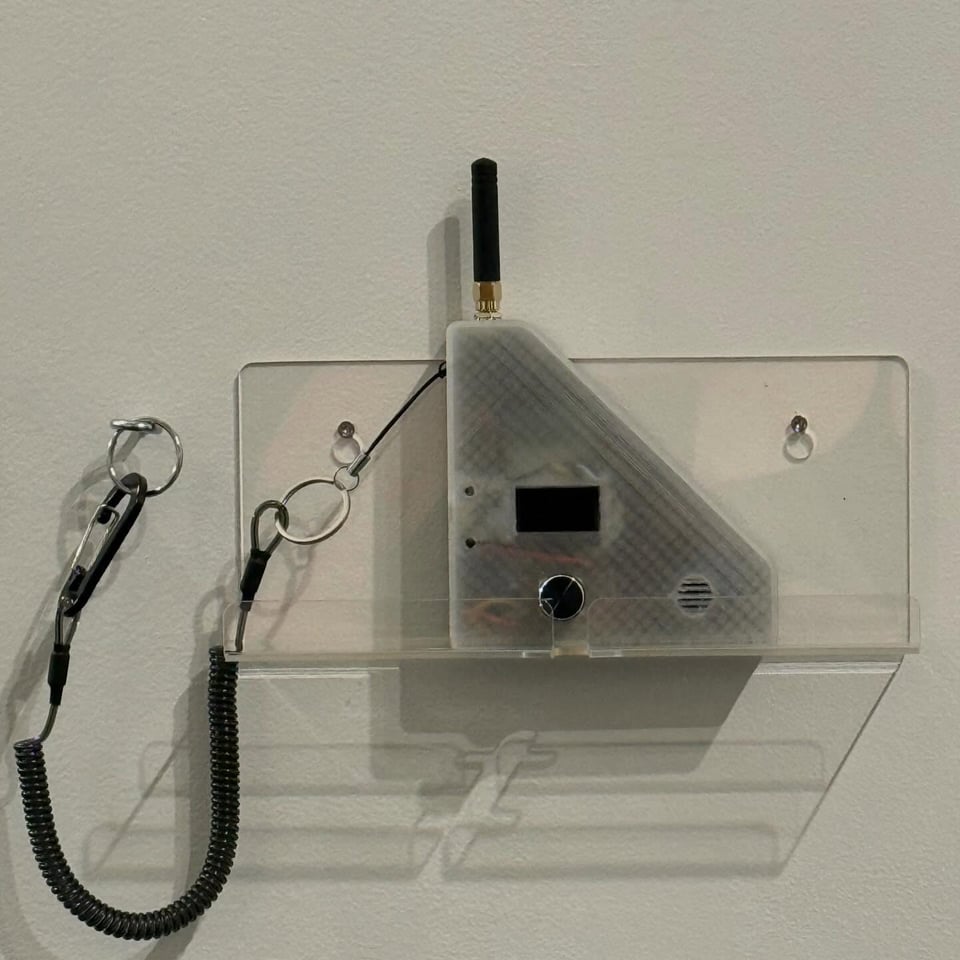 a translucent plastic device mounted on a clear acrylic shelf, attached to a carabiner with a curled wire coted in black plastic.