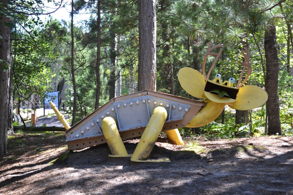 A metal sculpture of a dinosaur like creature with a gray body, yellow limbs and head, and very big ears.