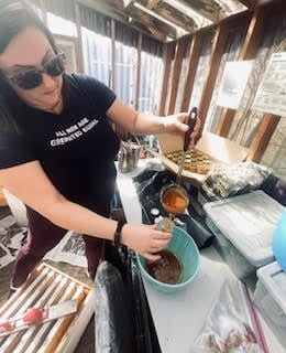 Your girl ladles honey from a bowl to a jar. (AI: "a woman preparing food in a greenhouse")