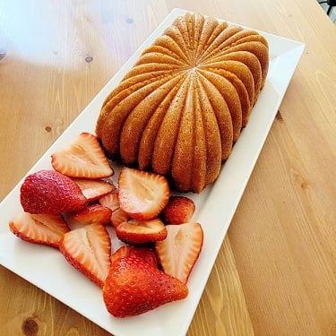 A loaf of pound cake on a white rectangular platter with sliced strawberries