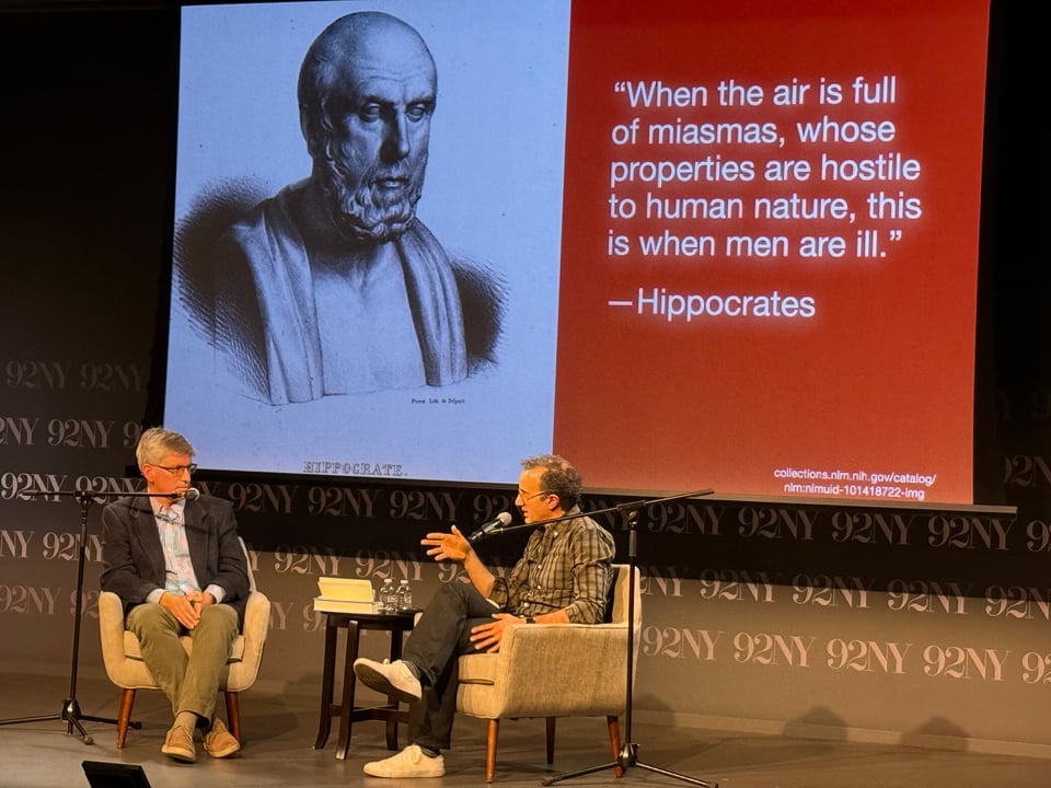 Jad Abumrad and I talking on stage about miasmas. A slide of Hippocrates looms behind us.