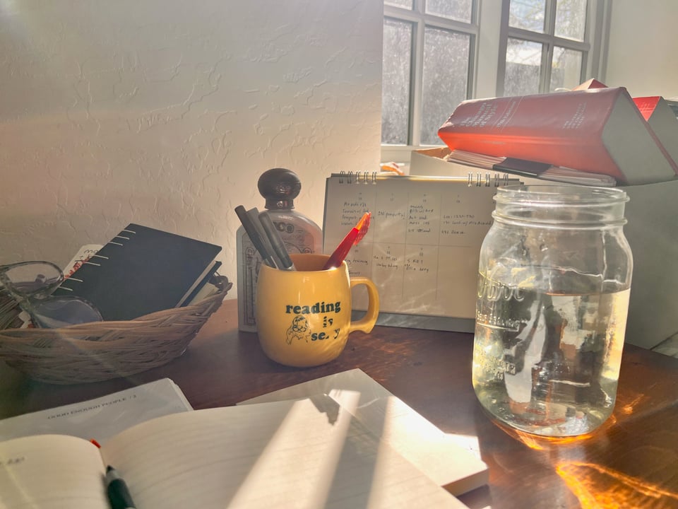 a snapshot of my desk with the sun coming in behind my mason jar of water