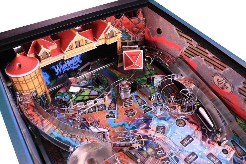 Image of the upper playfield of the pinball machine "Winchester Mystery House", featuring a small house toy and some ramps.