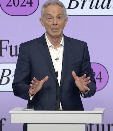 Tony Blair - a white man in his 70s, wearing a suit - against a purple background