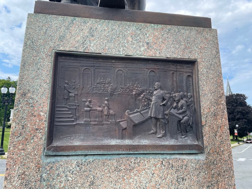A bronze plaque shows McKinley standing in the House chamber orchestrating passage of his tariff bill in 1890