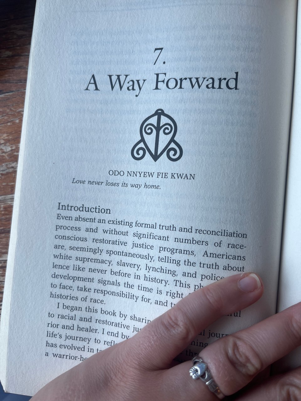 partial view of Nola's hand with upside-down Claddagh ring over a page of a book with the heading "A Way Forward," the Adinkra symbol and phrase for "odo nnyew fie kwan," and the English translation, "Love never loses its way home."