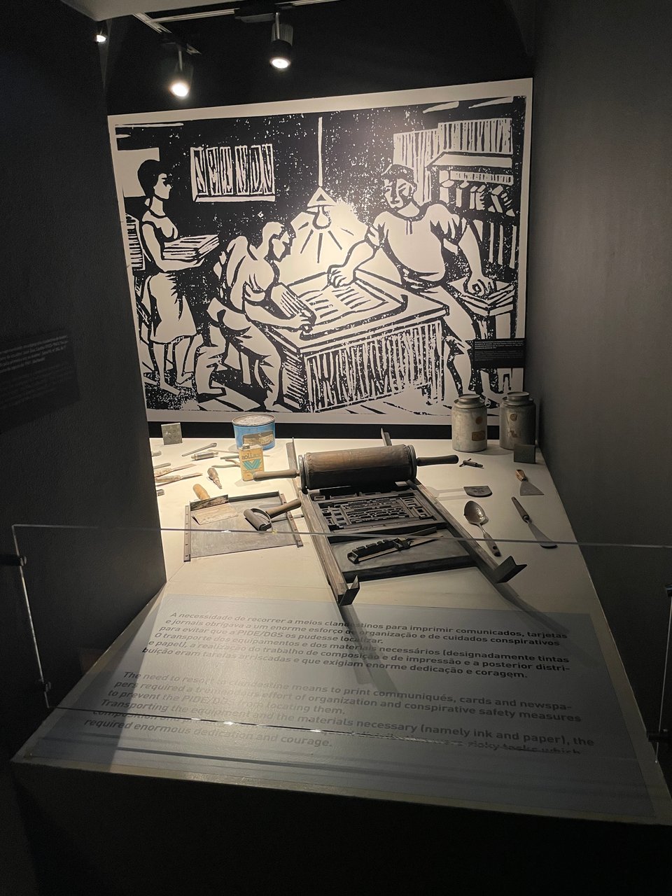 A museum display of a small printing press with tools and a painting of people using one to create underground newspapers.