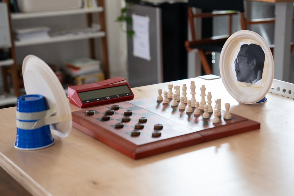 A crude effigy plays chess against a crude effigy playing checkers.