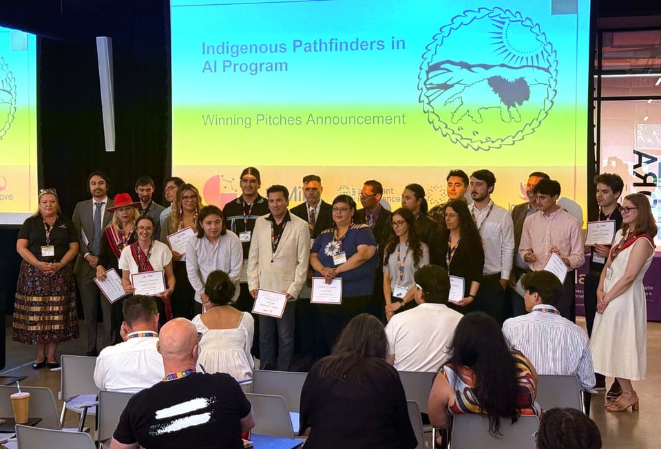 A group of Indigenous students and faculty stand two rows at the front of a conference room after receiving certificates of completion.