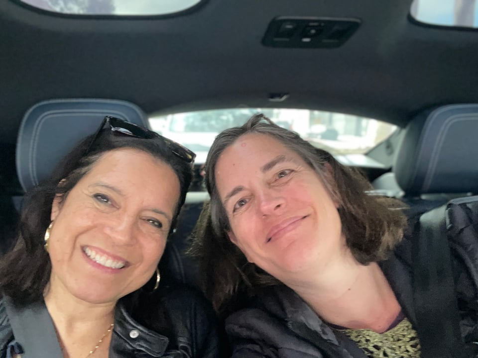 Two women sit in the back of a WAYMO taxi and smile at the camera.