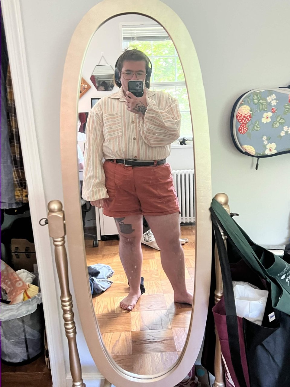 The artist standing in front of a gold mirror wearing a pink grey and white linen shirt with large puffy sleeves.