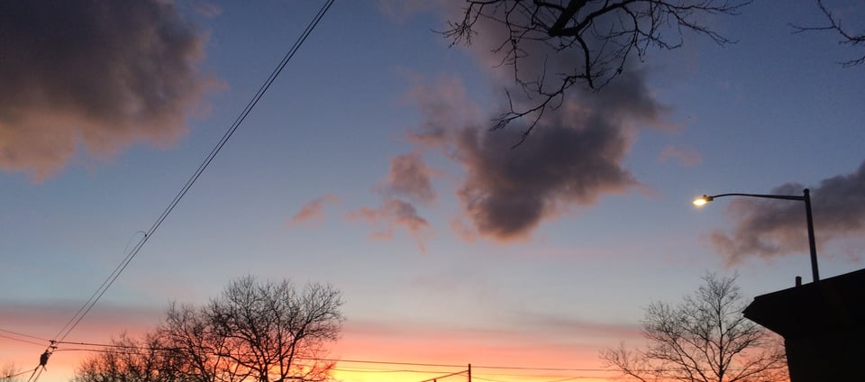 A photograph of the sky at dusk in Queens, New York, with telephone wires and street lights.