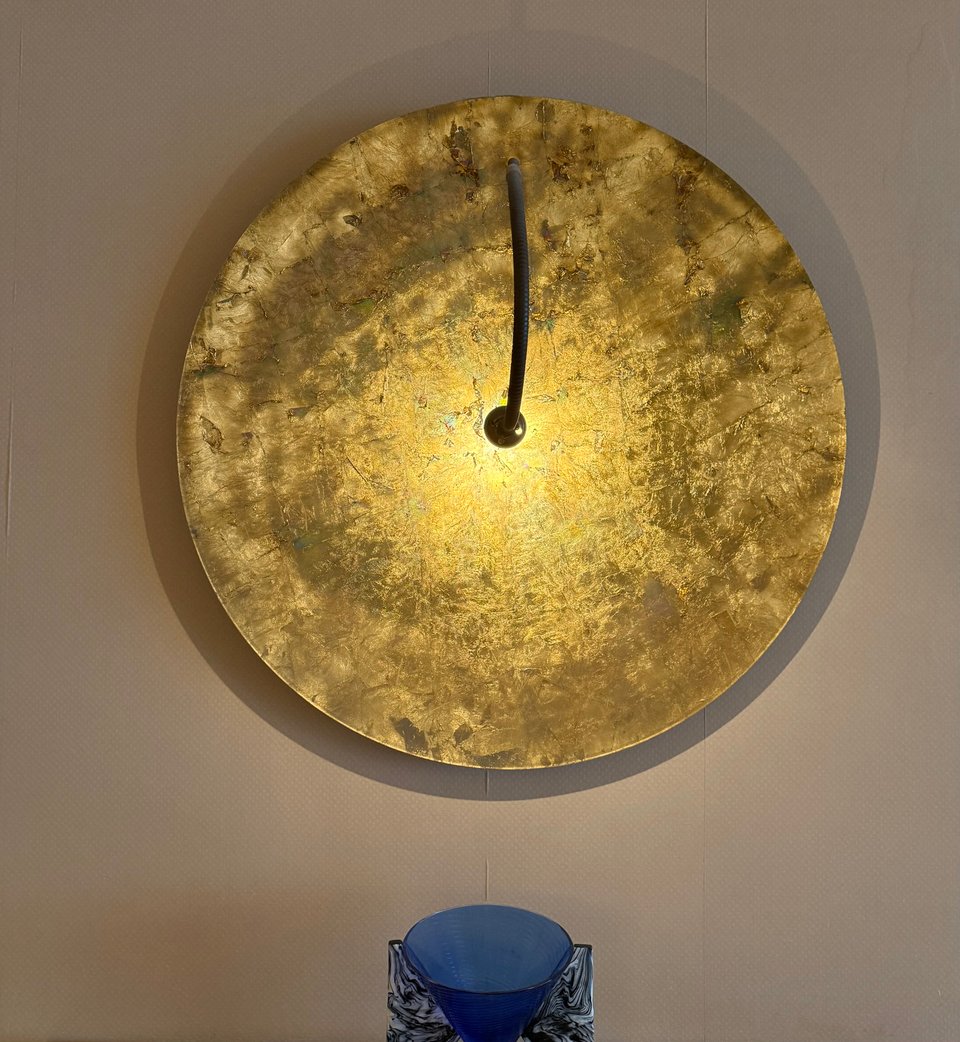 photo of large circular gold wall decoration with a lamp shining on the middle of it, with a blue glass container below, from the Royal Pines Hotel Urawa