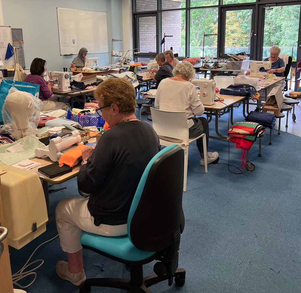 Scrubbery sewing room with many volunteers working on sewing machines