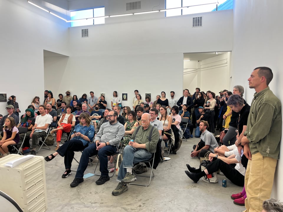 Crowd of people sitting and standing in a white room with some skylights. They're about to see some readings!!!