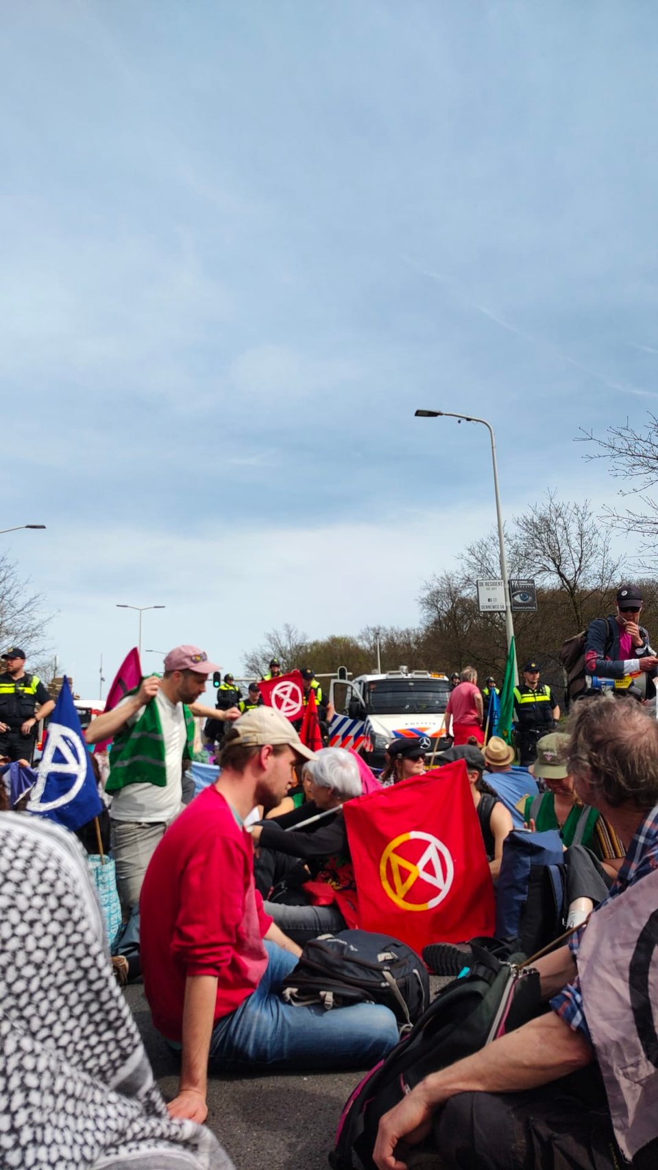 people sitting on a street, police in the background. The activists are holding flags with an hourglass in a circle