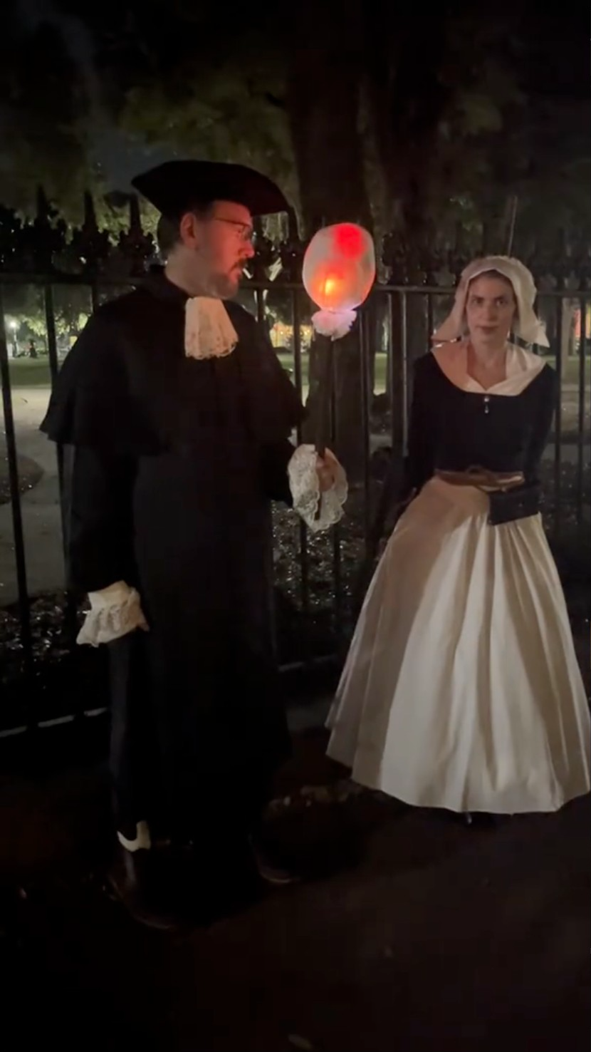 Two people dressed as American Puritans. The man holds a torch with an electronic flame
