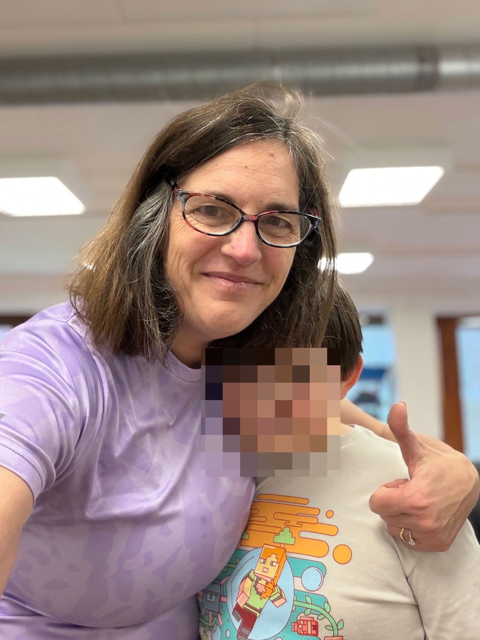 A woman and her son face the camera giving thumbs up and hug. His face is blurred.