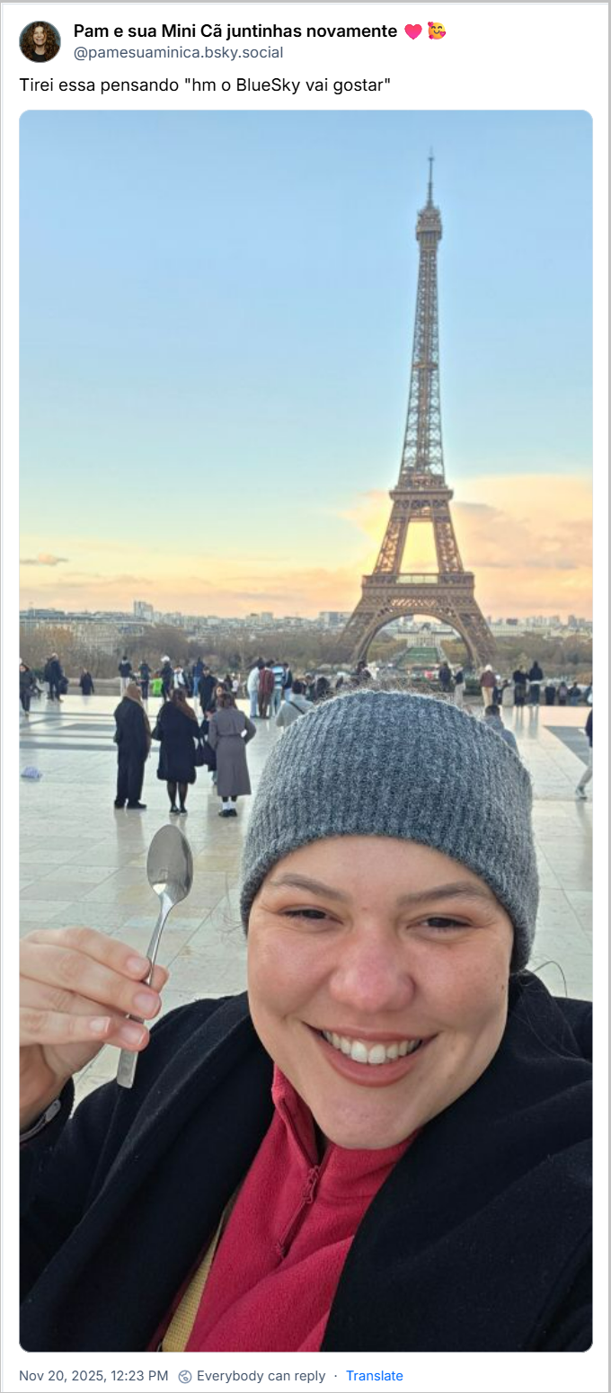 Post de Pam e sua Mini Cã juntinhas novamente ♥️🥰 (@pamesuaminica.bsky.social) com o texto: Tirei essa pensando "hm o BlueSky vai gostar" (imagem de uma moça sorridente, bem agasalhada e com gorro, em frente à Torre Eiffel, segurando uma colher)