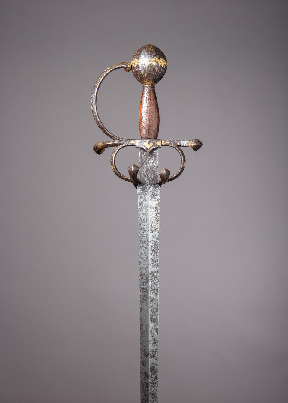 A photograph of the hilt and part of the blade of a sword. The hilt is spare but graceful, with a large, spherical pommel painted with gold diamonds around the equator and gold longitudinal lines. The grip appears to be covered with brown leather.