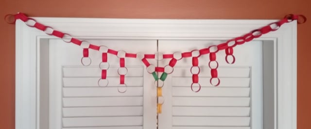 A chain made of links or red, green, and yellow paper hands in front of a white door. The center is a V pattern linking to itself.