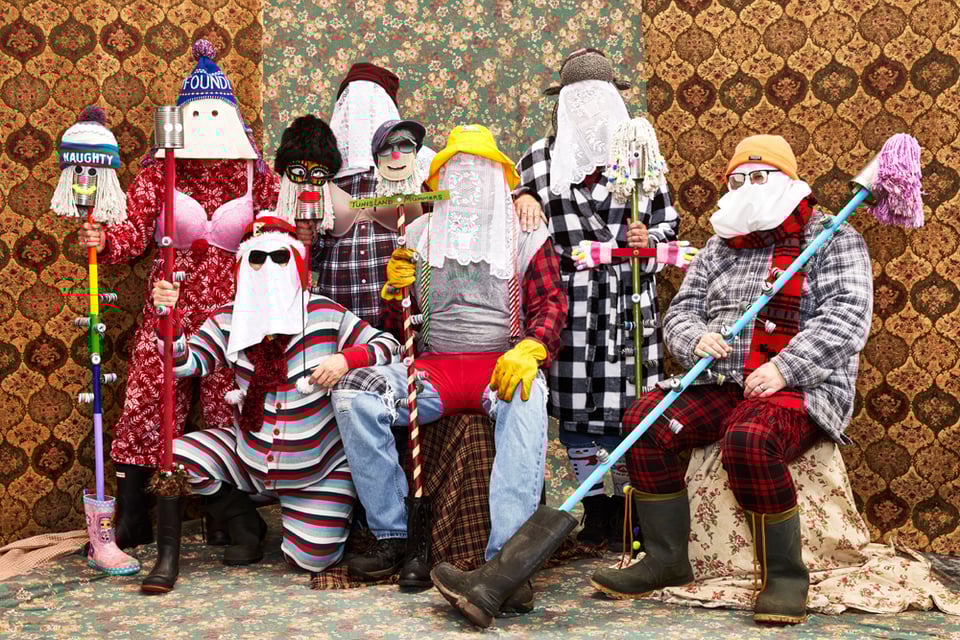 Eight mummers with white cloths and hoods over their faces, brightly coloured clothing, underwear as outerwear, and mops and ugly sticks to bang on the floor as instruments accompanying their clamourous singing. Photograph by Adam Coish