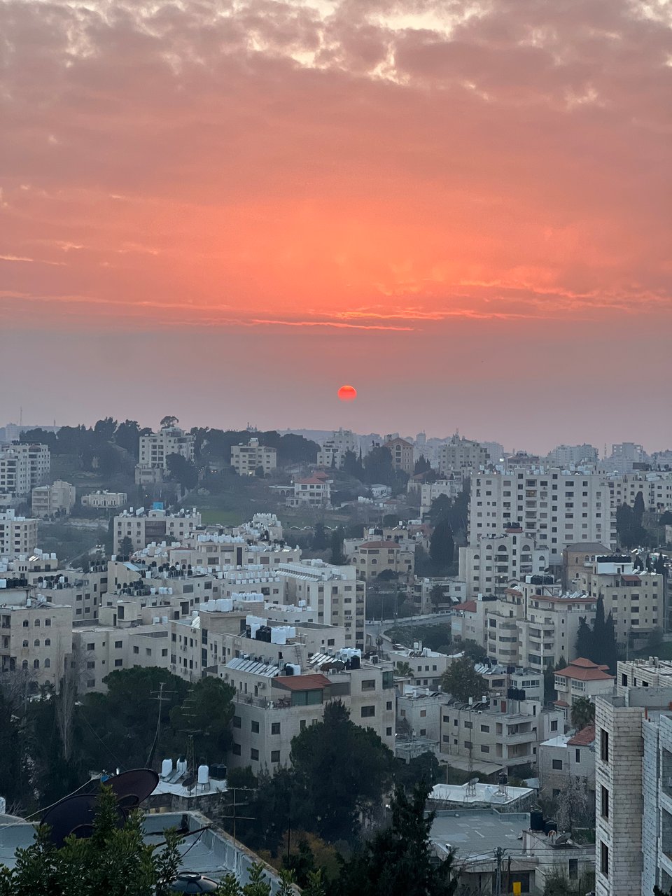 Aerial view of a city with white tall and medium-size buildings, an orange sky and a bright orange setting sun