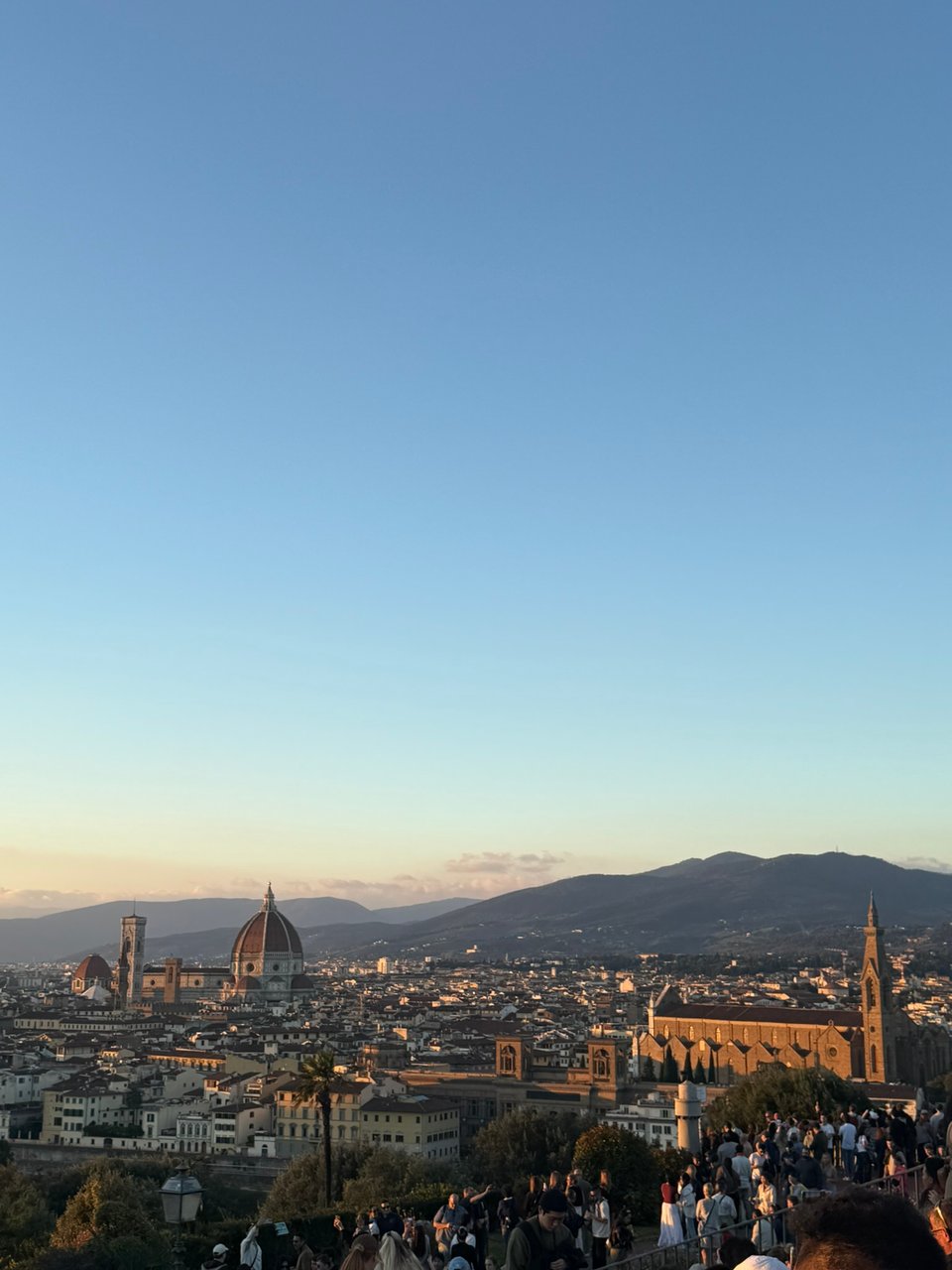A cityscape showing Florence at sunset, with the cathedral dome and surrounding hills visible under a clear sky.