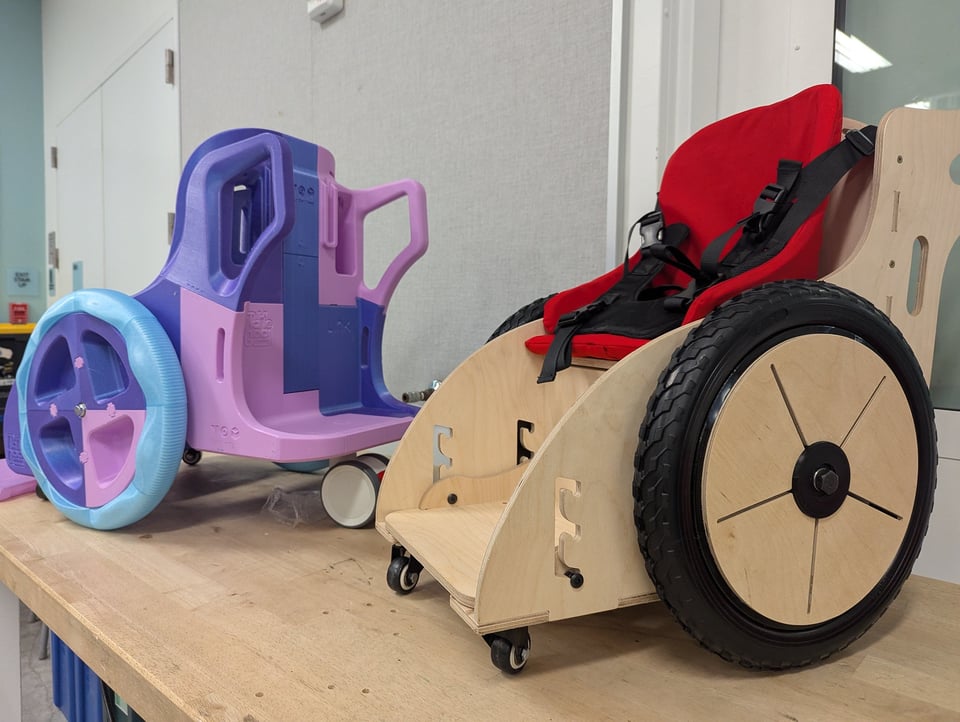 A toddler sized 3d printed and a plywood wheelchair next to each other
