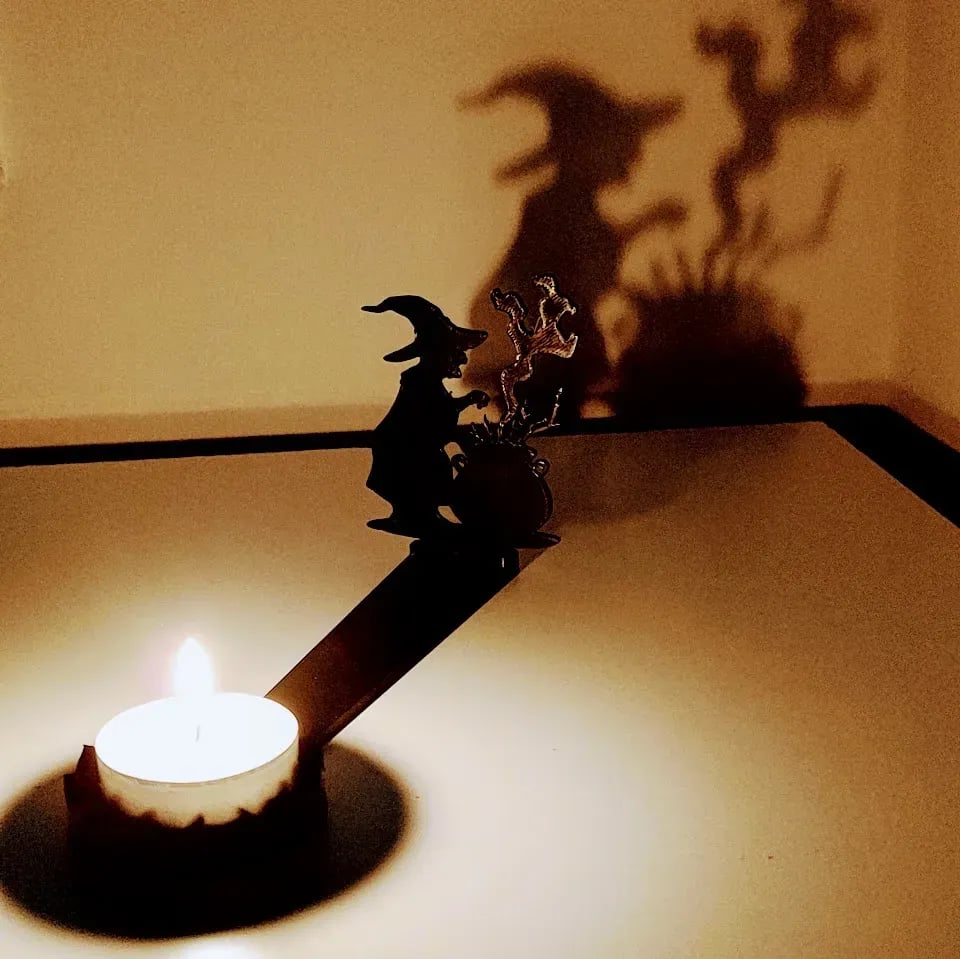 A tea light casts a shadow of a witch over a cauldron