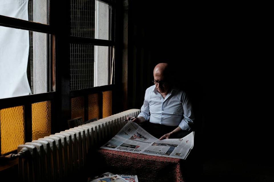 A stack of newspapers, on a table, as seen through a window. Photo by Mathias Reding on Unsplash.