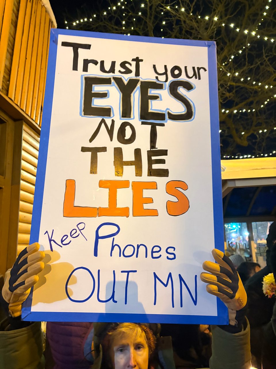Protester in Minneapolis holding up a sign that reads: "Trust your EYES not the LIES, Keep Phones out MN."