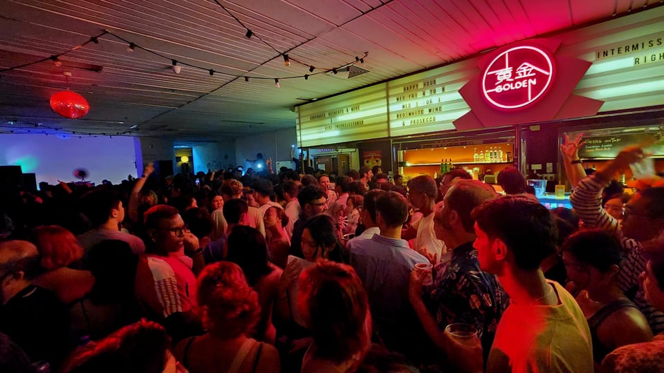 A crowd dancing in front of the signs for The Intermission Bar within The Projector.
