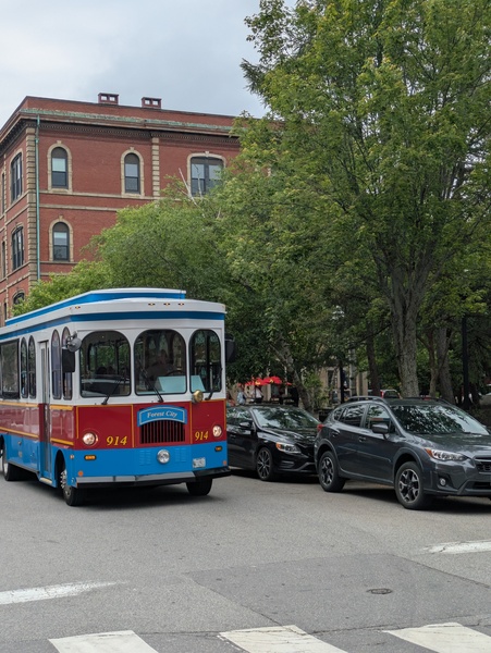a colorful, old-timey-looking bus drives down a street flanking a park in Portland, ME