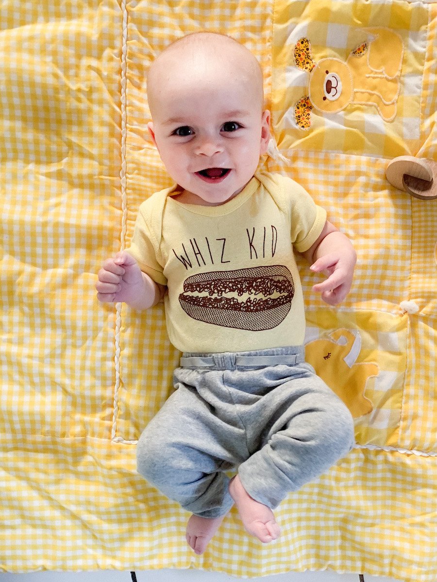 A smiling 6 month old baby lies on a blanket