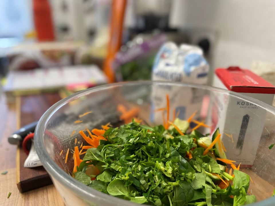 Green leaves and vegetables in a bowl with mess in the background
