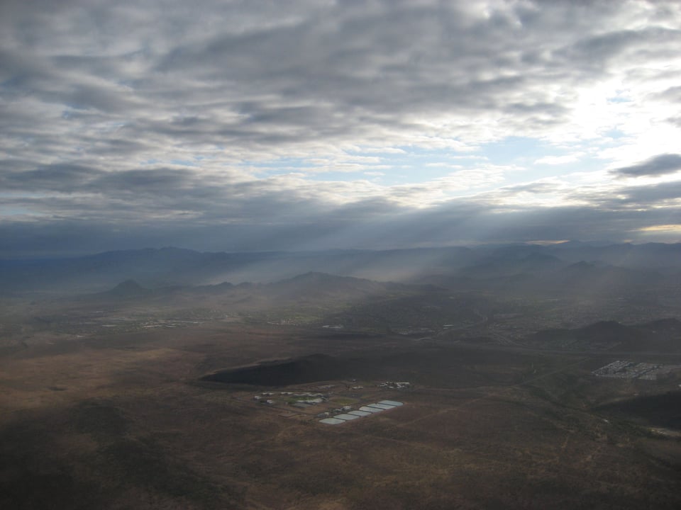 An aerial view of the desert, with slanting light from a hole in the clouds casting an otherworldly effect.