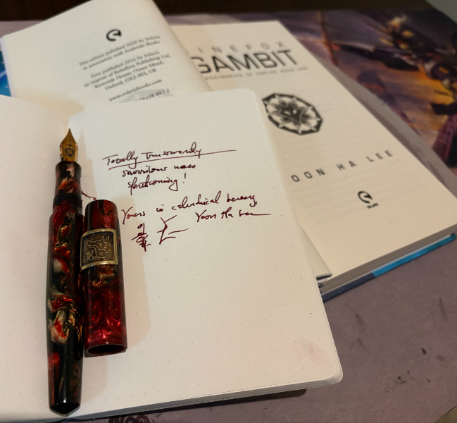 Ninefox Gambit and a notebook with the handwritten text "Totally trustworthy scurrilous notes forthcoming! Yours in calendrical heresy, Yoon Ha Lee" and a fountain pen