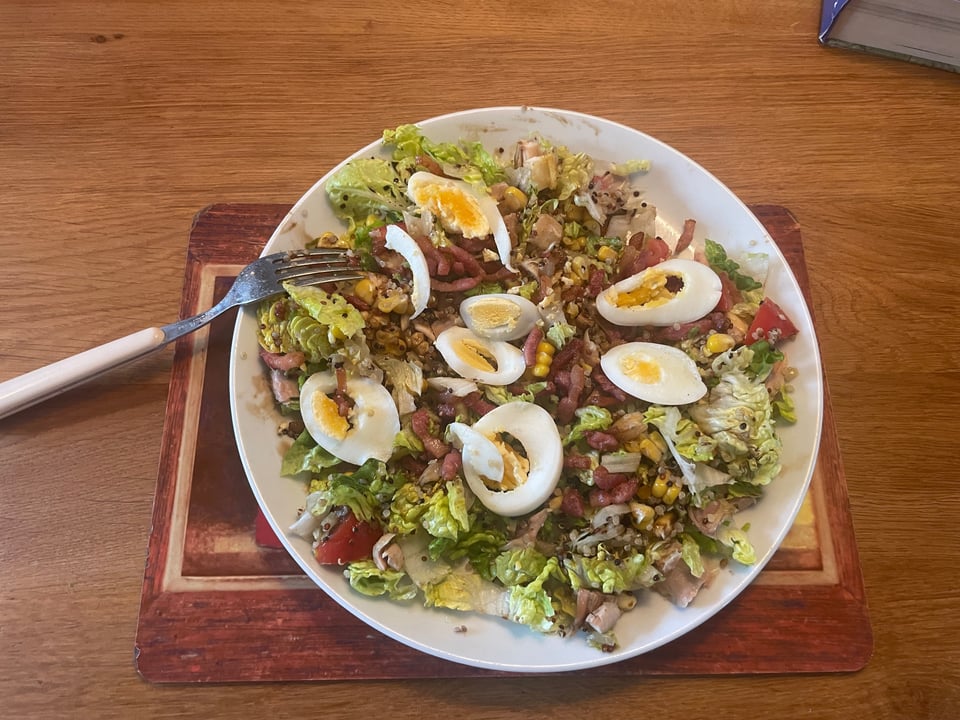 A plate of salad with egg and bacon bits, lettuce, tomato.