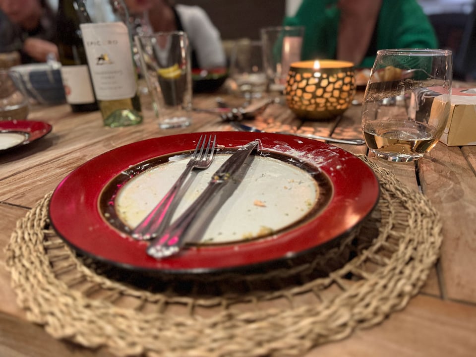 A fork and a knife are on top of an empty plate surrounded by glasses and a candle.