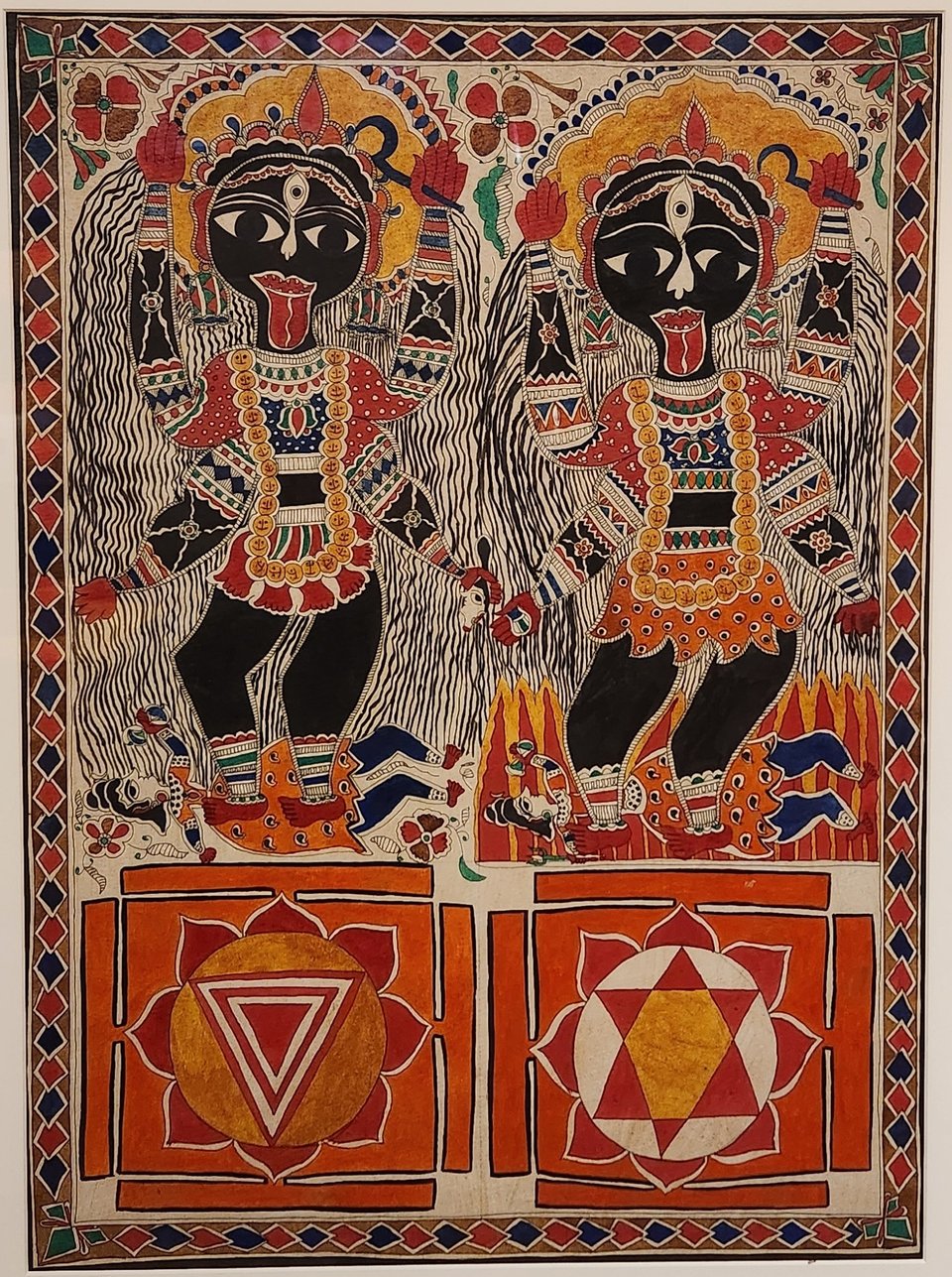 Two figures of Kali Ma in black, reds, oranges, yellows, and white, over different interpretations of her yantra