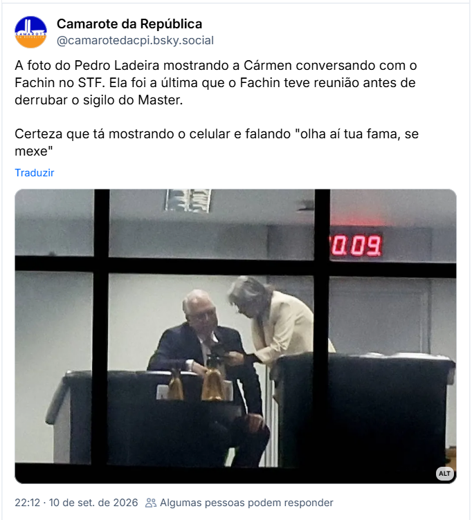 Post de Camarote da República (@camarotedacpi.bsky.social): A foto do Pedro Ladeira mostrando a Cármen conversando com o Fachin no STF. Ela foi a última que o Fachin teve reunião antes de derrubar o sigilo do Master. Certeza que tá mostrando o celular e falando "olha aí tua fama, se mexe"
(Foto de Cármen Lúcia e Edson Fachin, Ministros do Supremo Tribunal Federal, vista através das divisórias de uma janela de vidro. À esquerda, Edson Fachin está sentado vestindo terno escuro e camisa social clara, com a cabeça levemente inclinada. À direita, Cármen Lúcia está em pé, vestindo um blazer claro, inclinando-se para conversar com ele e mostrando a tela de um celular ou objeto em suas mãos. Ao fundo, na parede superior direita, sobressai um relógio digital com marcadores em luz vermelha. Foto: Pedro Ladeira.)