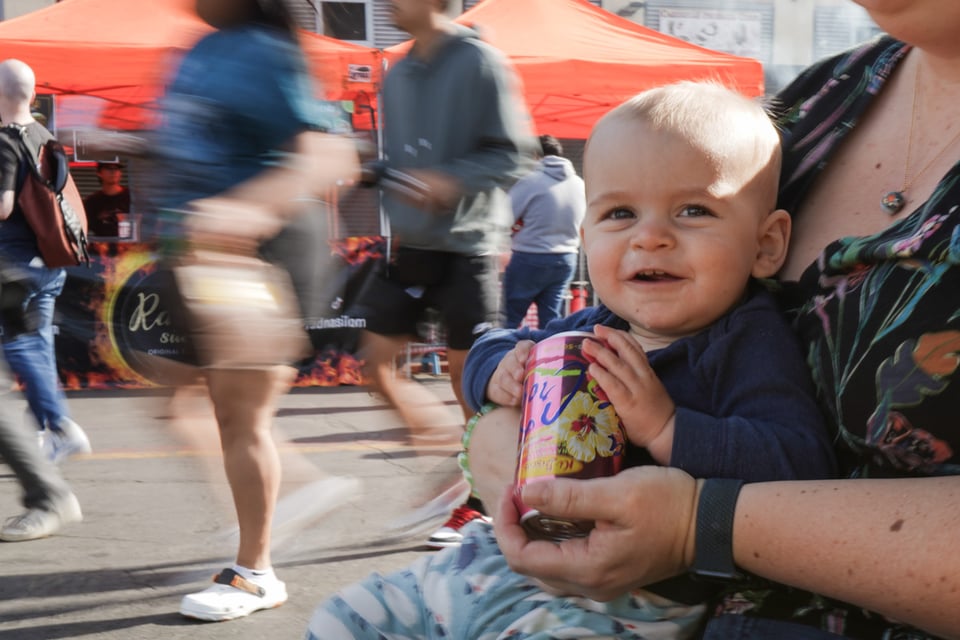 A baby sits on someone's lap as people walk by at a food festival