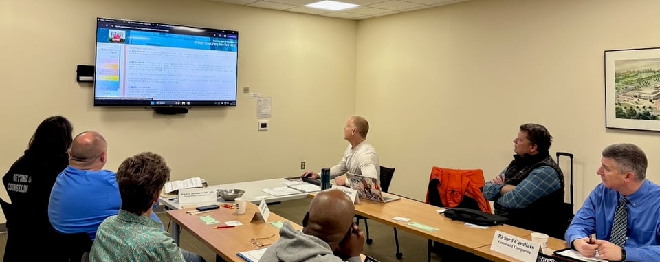Tom is seated in front of NRG members while using a mouse to highlight his home inspection online reporting system he uses.