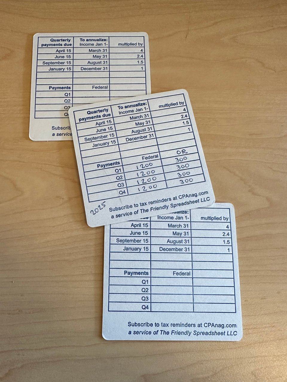 Off white coasters with navy ink are printed with a spreadsheet that lists when quarterly payments are due, explain how to annualize income at each deadline, and have a 'fill in the blank' section to write in one's own payments.