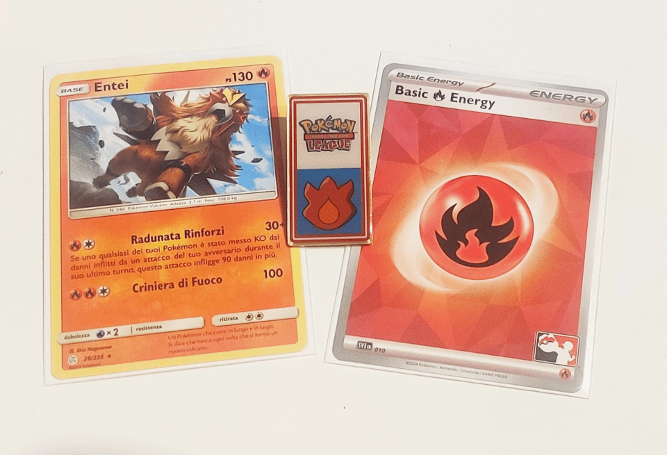An Italian Entei Pokémon TCG card, a basic Fire energy card and a Pokémon TCG League Volcano Badge