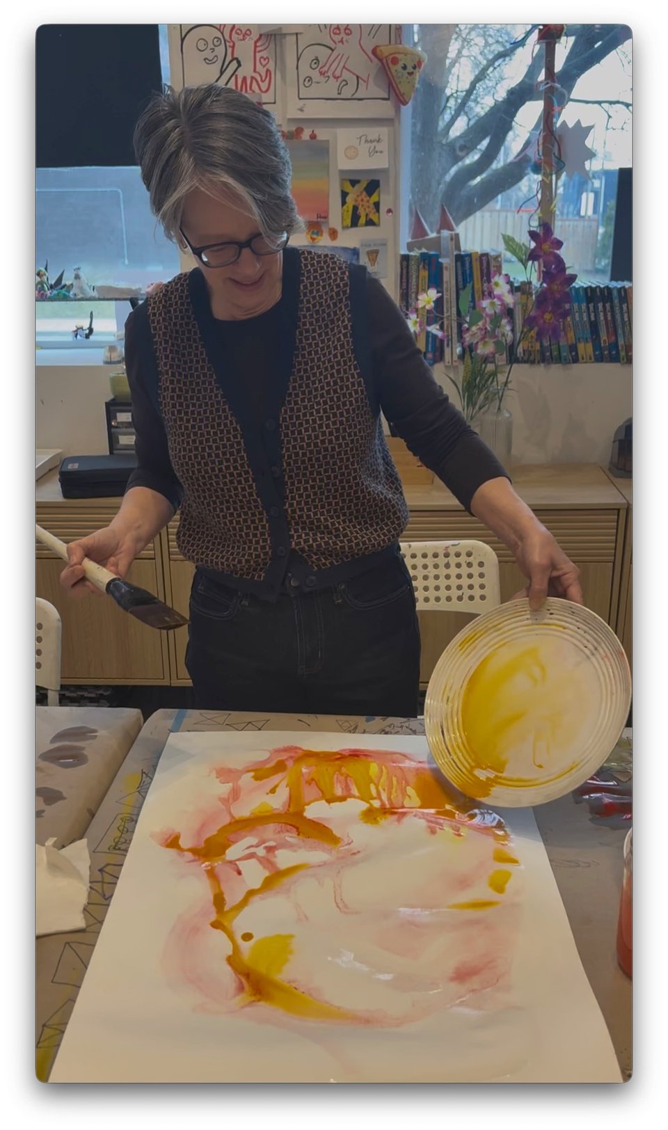 A woman with short hair pouring paint off of a plate onto a large sheet of paper